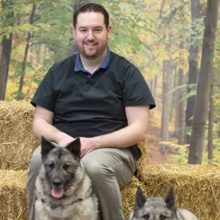 Dr. Jeff Brisebois sitting on hay with two dogs